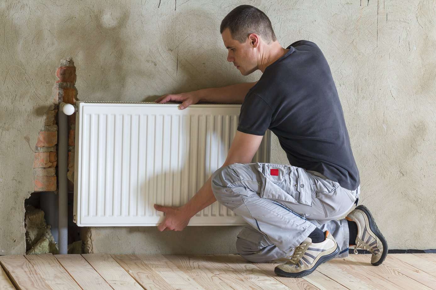 Young handsome professional plumber worker installing heating radiator